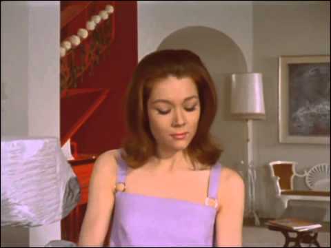 Youtube video showing Emma entering her flat wearing a pale lavender sun dress. She sees a box of chocolates has been left inside the cavity of her sculpture but opening it reveals nothing but Steed’s signature summons card which reads ‘Mrs. Peel WE’RE NEEDED!’