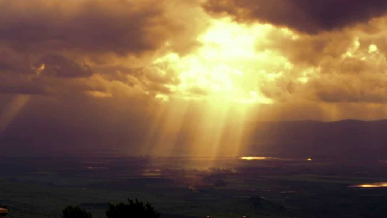 Stock Video Footage of sun rays illuminating a valley through clouds