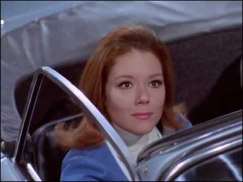 Youtube video - Mrs. Peel is stopped at some traffic lights. When they turn amber, the light has ‘MRS. PEEL’ taped on it and the go light reveals ‘WE’RE NEEDED’. She turns to find Steed in his Bentley behind her, doffing his hat