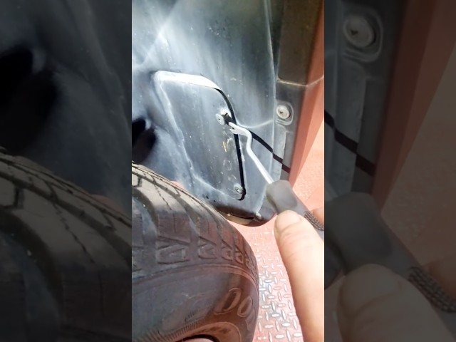 a mechanic working on a car's wheel well, specifically using a trim removal tool to access the area