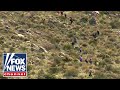 Migrants scale mountain like trail of ants to get into US
